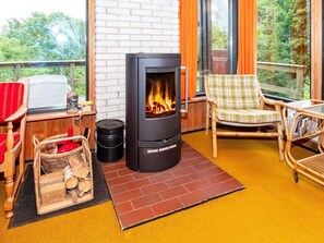 A cozy room with a wood-burning stove, wicker furniture, and a view of the outdoors. - Lovely Holiday Home in SpÃ¸ttrup near Sea (Spøttrup)