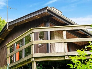 Une cabane en bois dotée d’un balcon, d’une cheminée et d’une fenêtre donnant sur la forêt.