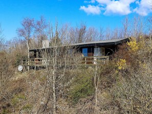 A cabin with a wooden deck and a large window, surrounded by dense shrubbery and trees. - Lovely Holiday Home in SpÃ¸ttrup near Sea (Spøttrup)