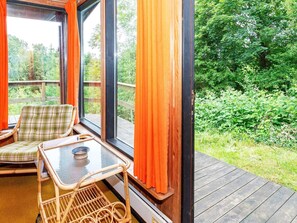 A room with a wicker chair, a small table, and a view of a wooded area through large windows. - Lovely Holiday Home in SpÃ¸ttrup near Sea (Spøttrup)