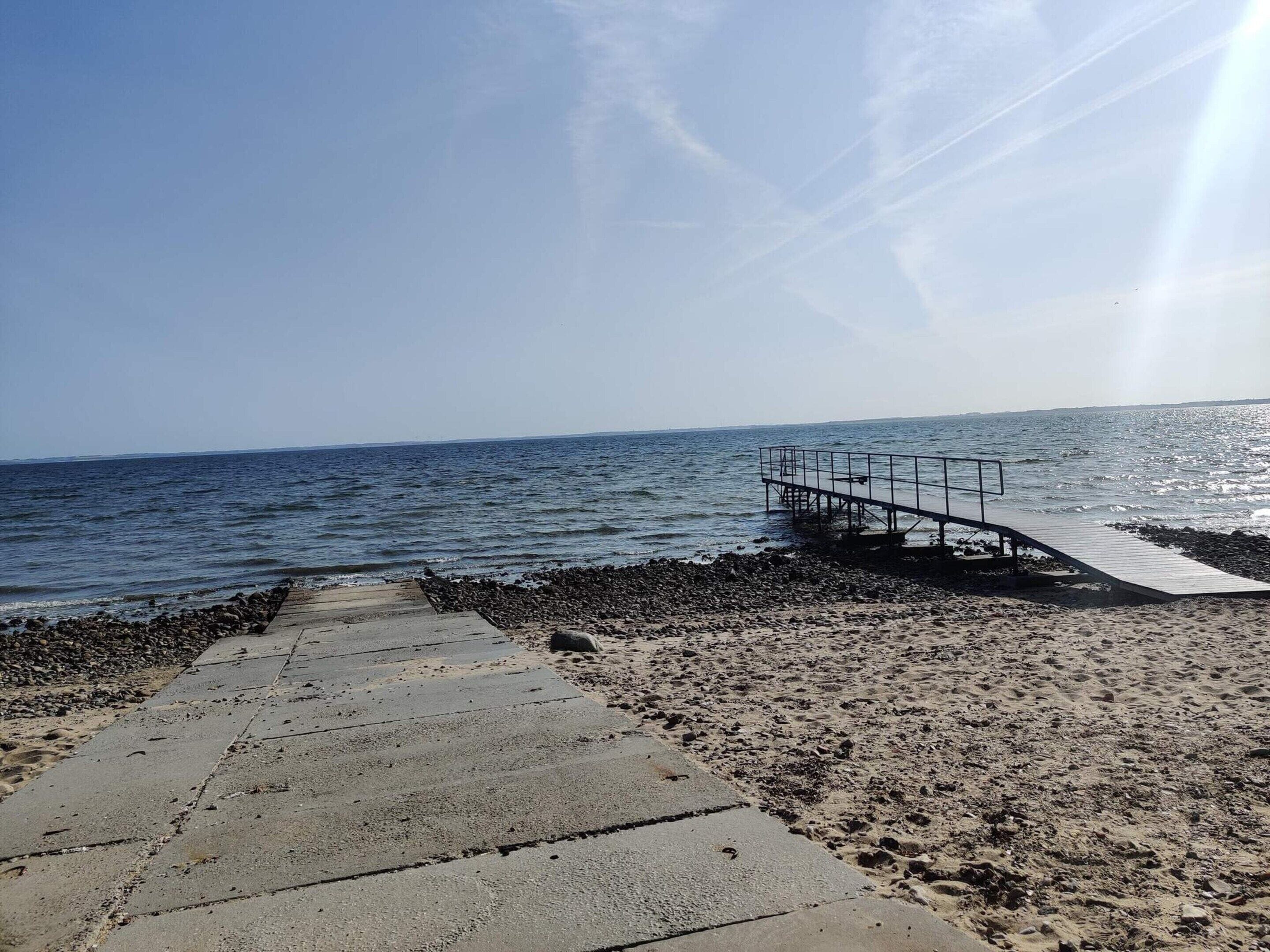 A concrete pathway leading to a pier extending into calm waters, with a clear sky above.