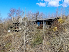 A cabin with a wooden deck and a large window, surrounded by dense shrubbery and trees. - Lovely Holiday Home in SpÃ¸ttrup near Sea (Spøttrup)