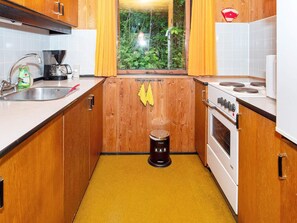 A compact kitchen with wooden cabinets, a sink, a stove, and a window with curtains. - Lovely Holiday Home in SpÃ¸ttrup near Sea (Spøttrup)