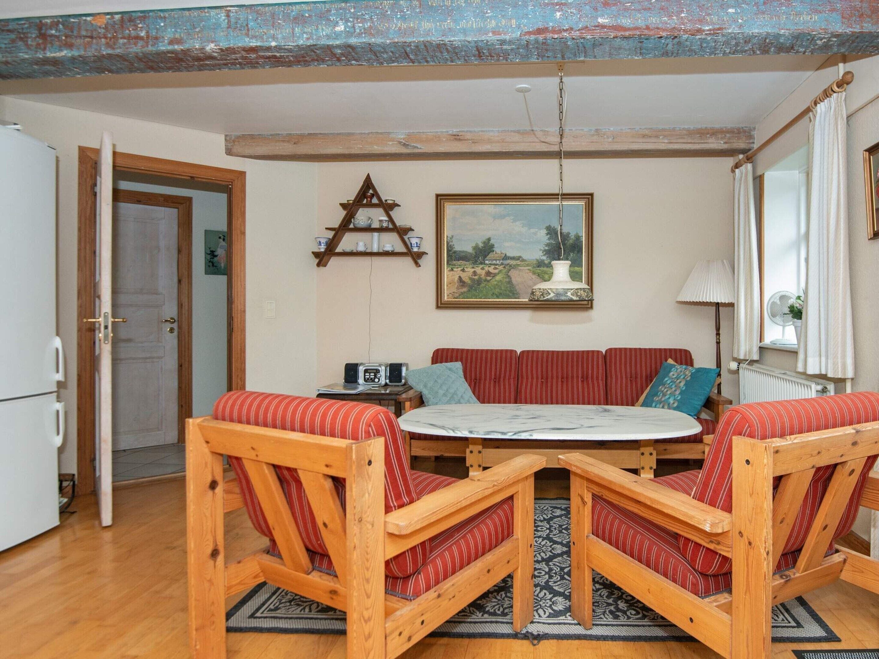 Et værelse med et træbord omgivet af fire stole, en rød-stribet sofa, et billede på væggen og en hvid radiator.