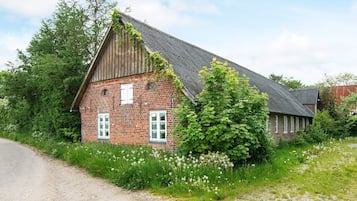 A rustic brick building with a sloped roof, surrounded by lush greenery and wildflowers.