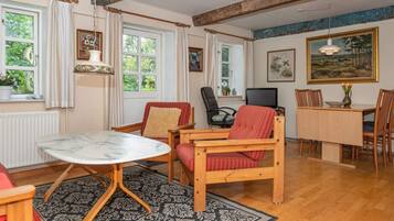 Uma sala de estar acolhedora com uma mesa de jantar de madeira, uma poltrona confortável, um sofá e uma televisão.