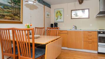 A dining area with wooden chairs and a table, a kitchen with wooden cabinets and a stove, and artwork on the walls.
