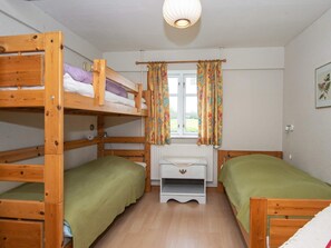 Een slaapkamer met een stapelbed, raam, gordijnen en een radiator.