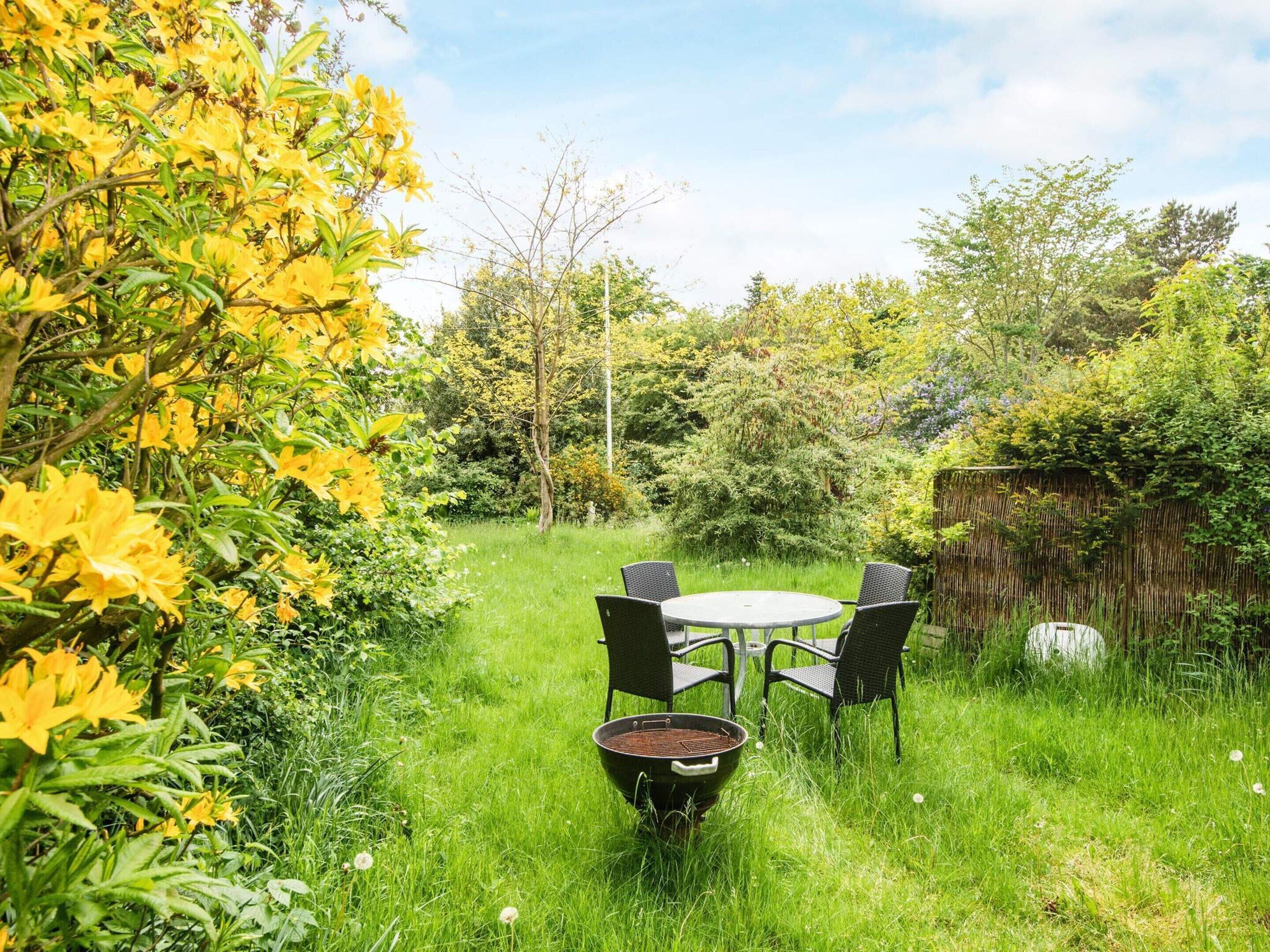 An outdoor seating area with a round table and four chairs, surrounded by lush greenery and yellow flowers.