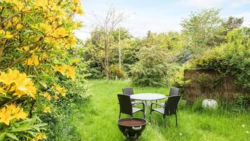 An outdoor seating area with a round table and four chairs, surrounded by lush greenery and yellow flowers.