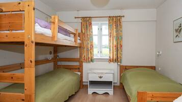 A bunk bed room with a window, curtains, and a radiator.