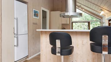 A kitchen with wooden walls, a stainless steel range hood, a white refrigerator, and two black bar stools.