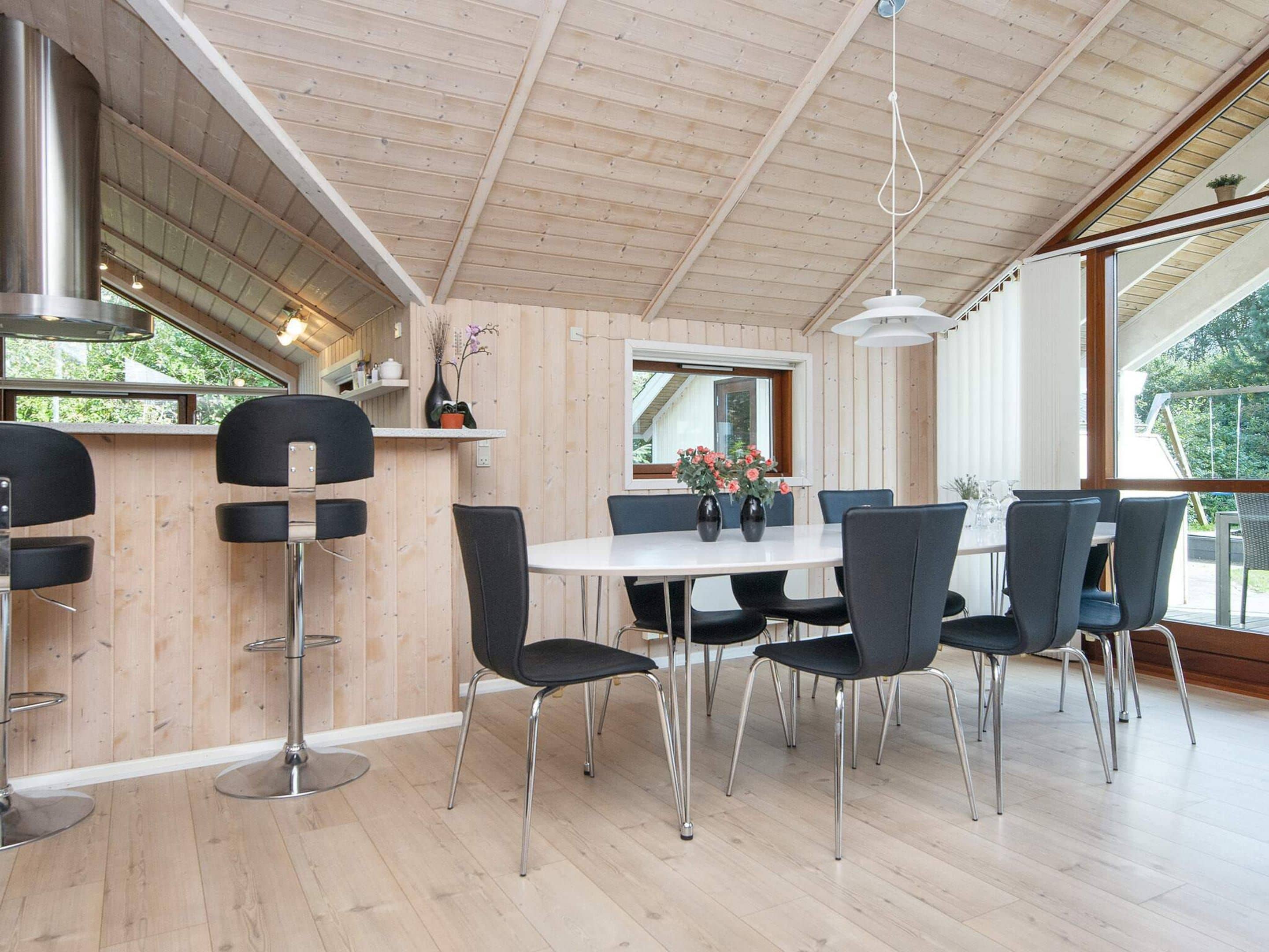 A modern dining area with a wooden ceiling, a white table, and black chairs.