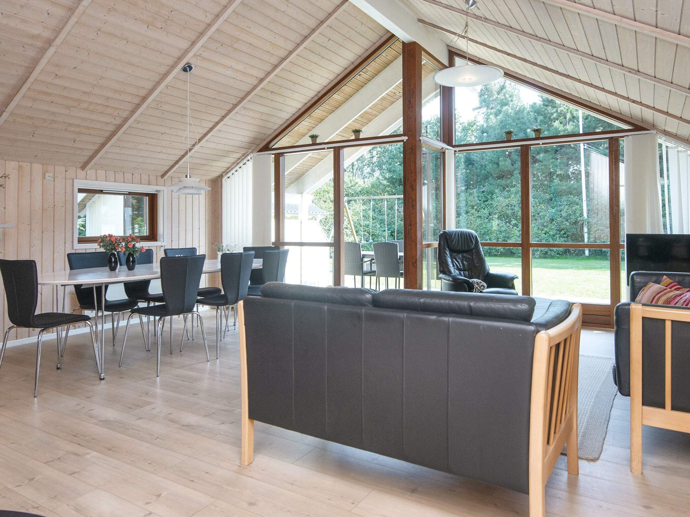 A spacious room with a high ceiling, large windows, a dining area with chairs, and a sofa.