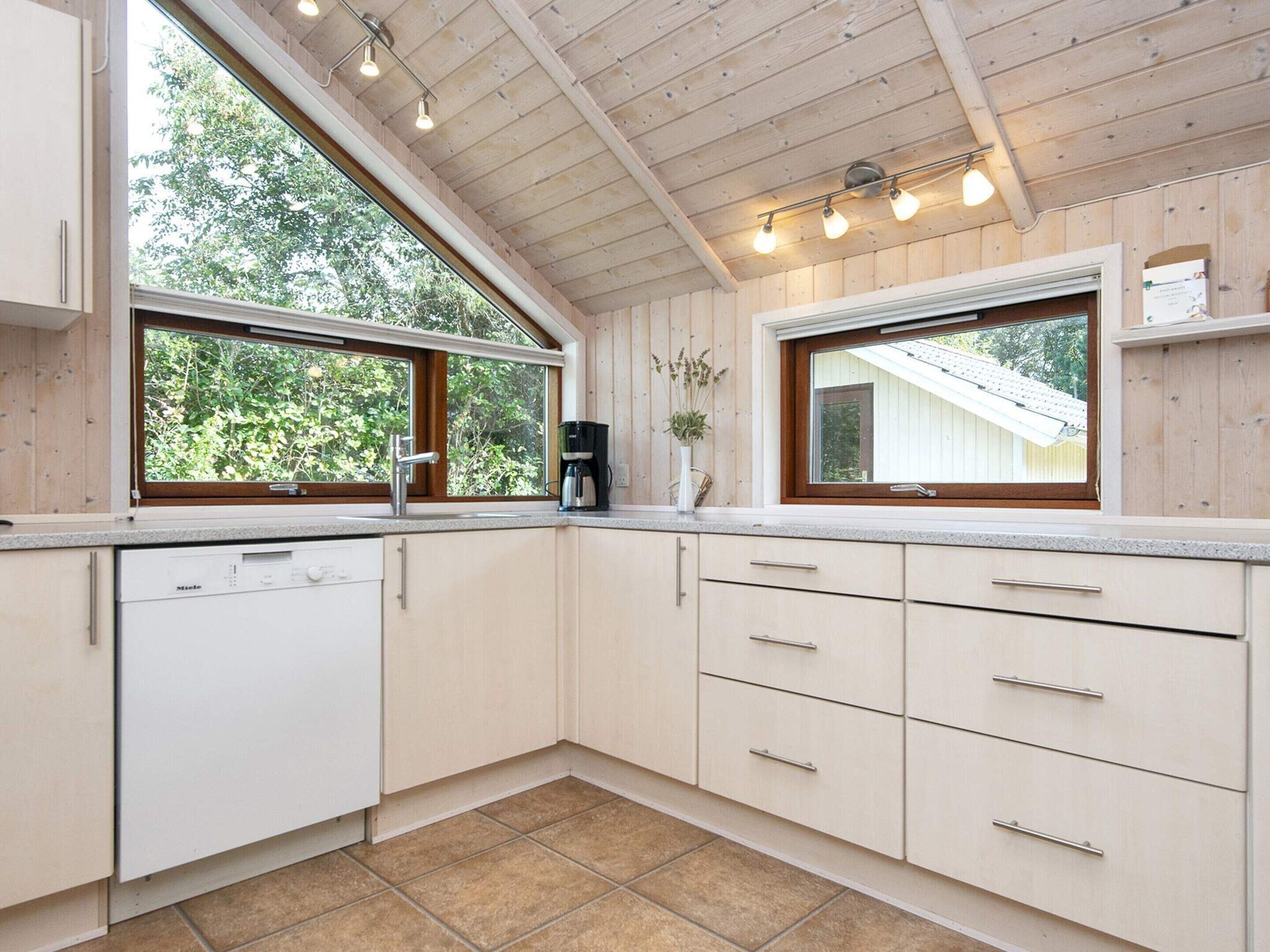 A modern kitchen with wooden cabinets, a dishwasher, and two windows providing natural light.
