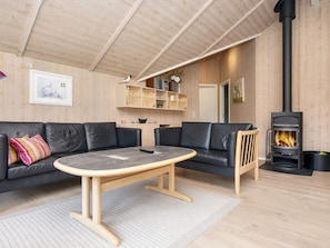 A cozy living room with a sofa, a coffee table, a fireplace, and wooden walls. - 5 Star Holiday Home in Ulfborg (Ulfborg)