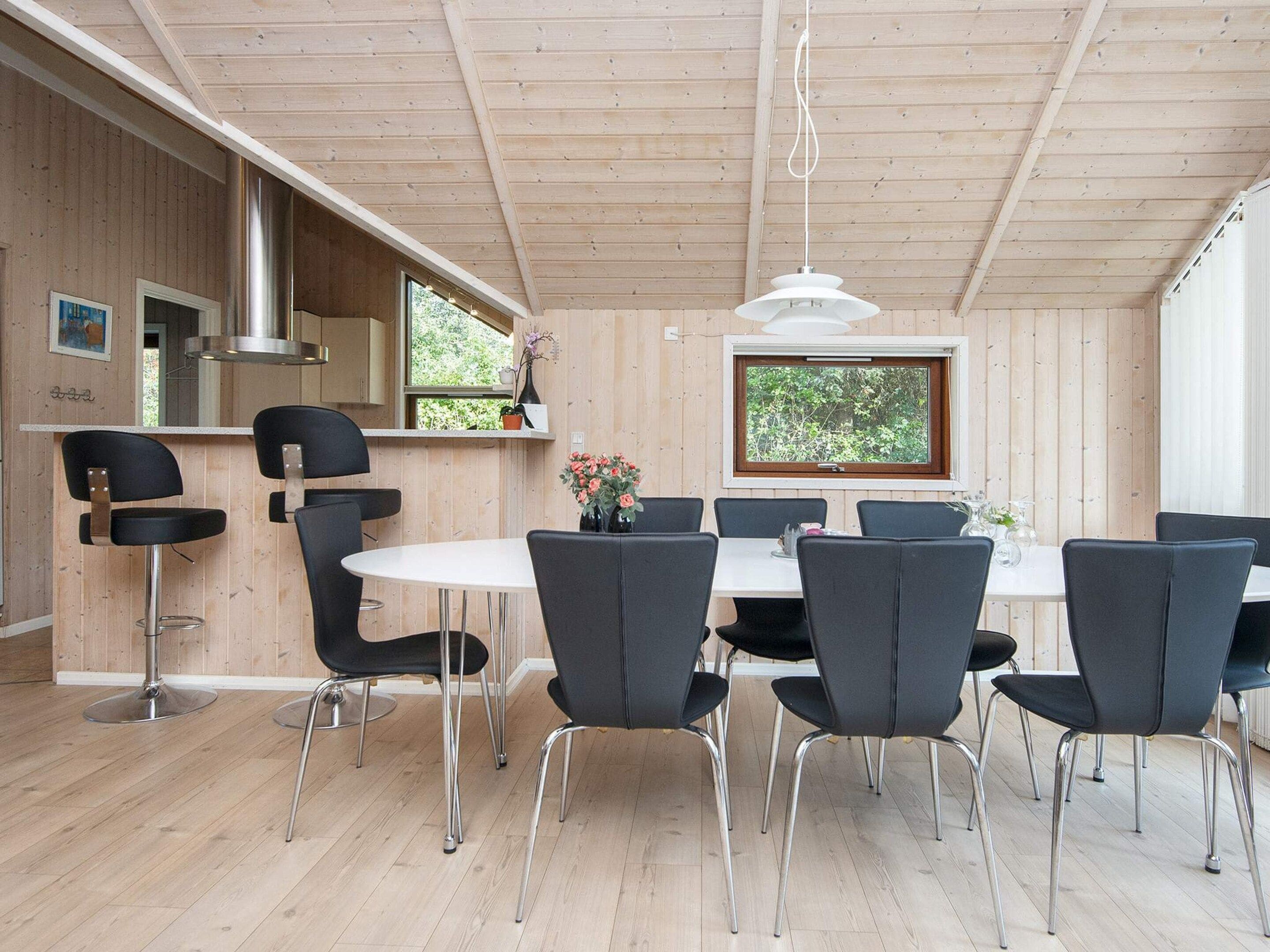 Een modern interieur met een houten plafond, een ronde eettafel met stoelen, een keuken met een fornuis en een raam met uitzicht op groen.