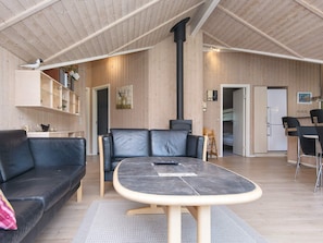 A modern interior with a sofa, a table, a fireplace, and a kitchen area. - 5 Star Holiday Home in Ulfborg (Ulfborg)