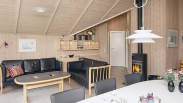 Una sala de estar acogedora con chimenea, paredes de madera, un sofá, una mesa de centro y un comedor.