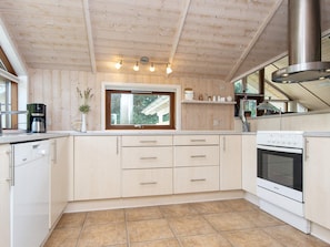 A modern kitchen with wooden cabinets, a built-in oven, and a window overlooking a house.
