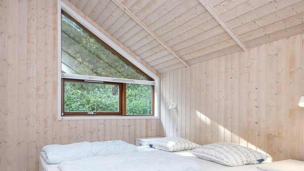 Un dormitorio con una cama, una mesita de noche, un ventanal y paredes de madera.