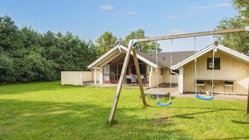 A residential property with a wooden swing set, a covered patio area, and a lawn.