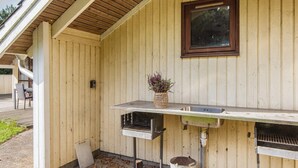 Fachada de madera con estación de parrilla metálica, una ventana y una jardinera con flores.