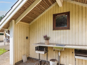 A wooden exterior with a metal grill station, a window, and a planter with flowers.