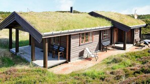 Una cabaña de madera con techo de hierba, un porche cubierto y un patio con mobiliario.