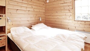 Una habitación de cabaña de madera con una cama, una mesita de noche, una lámpara y una ventana.