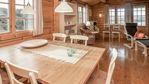 Interior de una cabaña de madera con una mesa de comedor, sillas y una chimenea.