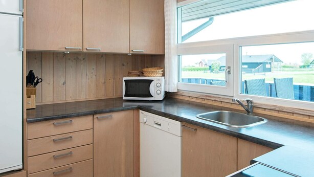 A modern kitchen with wooden cabinets, a microwave, a dishwasher, and a large window offering a view of the outdoors. - 6 Person Holiday Home in Sjolund-by Traum (Sjølund)