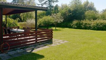 Un espace extérieur aménagé avec une table et des chaises, entouré d’une pelouse verdoyante et d’arbres.