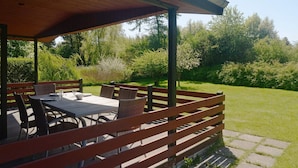 An outdoor patio with a table and chairs, surrounded by a wooden fence, overlooking a grassy area with trees. - 6 Person Holiday Home in Praesto (Praesto)