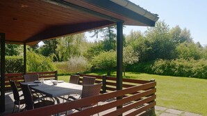 An outdoor patio with a table and chairs, surrounded by a wooden fence, set against a backdrop of greenery and trees. - 6 Person Holiday Home in Praesto (Praesto)