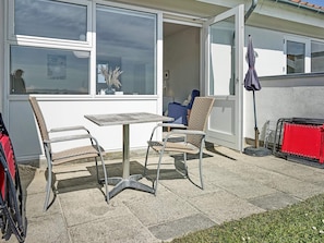 An outdoor patio with a table and two chairs, a red storage unit, and a blue chair.