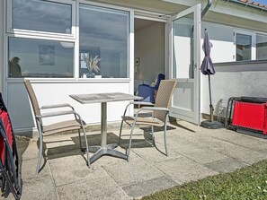 Een terras buiten met een tafel, twee stoelen, een rode opbergunit en een blauwe stoel.