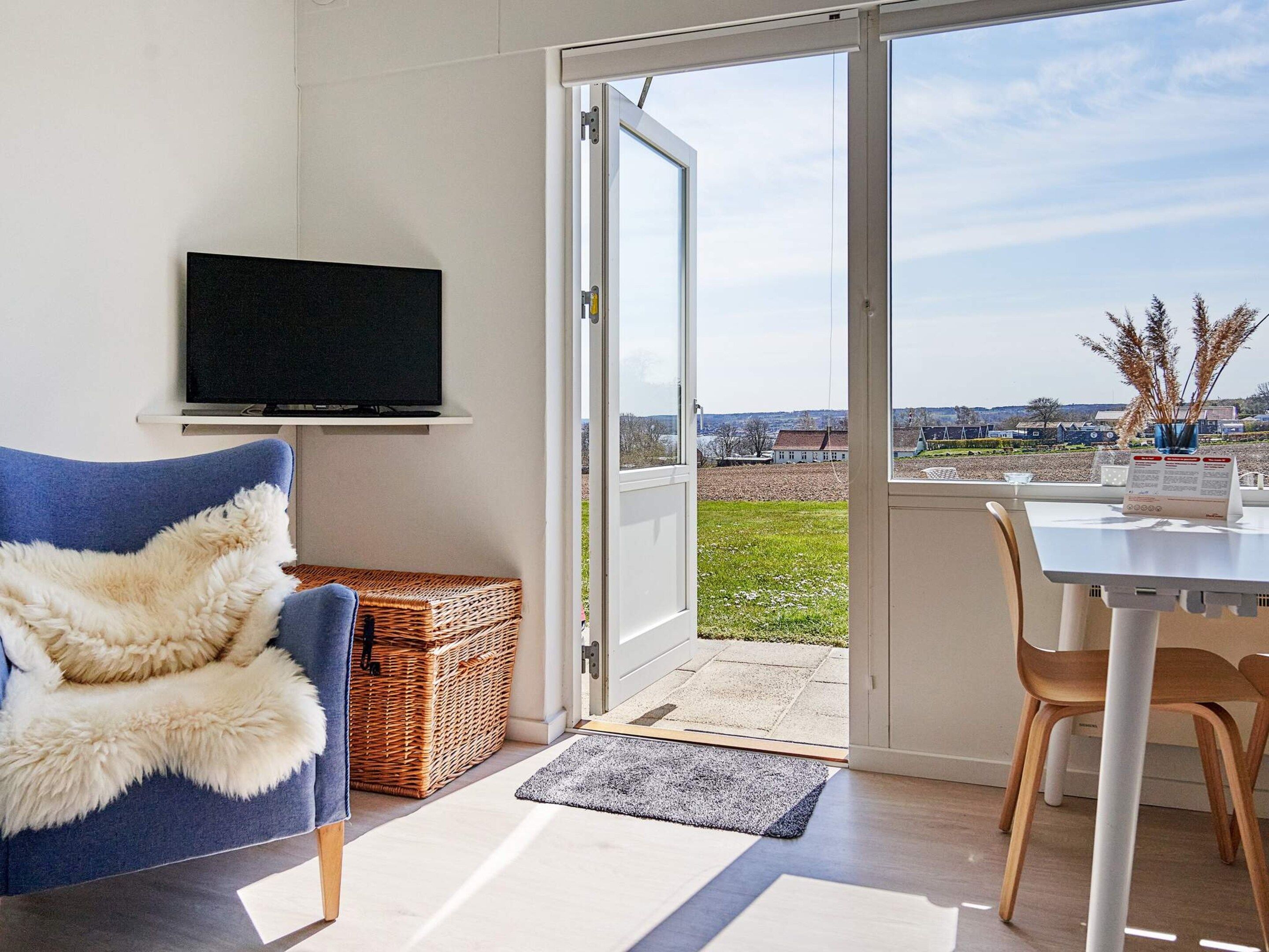 Una sala de estar moderna con una televisión, un sillón azul, una cesta de mimbre y un comedor con mesa y sillas.