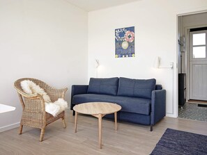 Een woonkamer met een bank, een rieten stoel, een klein rond tafeltje en een kunstwerk aan de muur.