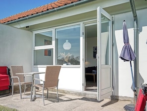 A room with a sliding glass door, wicker chairs, a red sofa, and a blue umbrella.