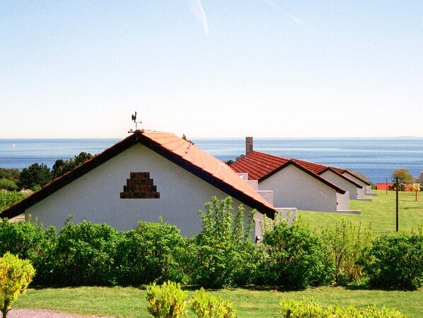 A row of white buildings with red roofs, a clear sky, and a view of the sea.