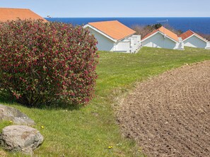 Una propiedad costera con edificios blancos, un arbusto con flores rosadas y una vista despejada del mar.