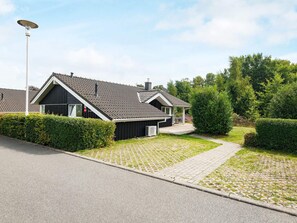A modern residential building with a sloped roof, a covered patio, and a paved driveway.