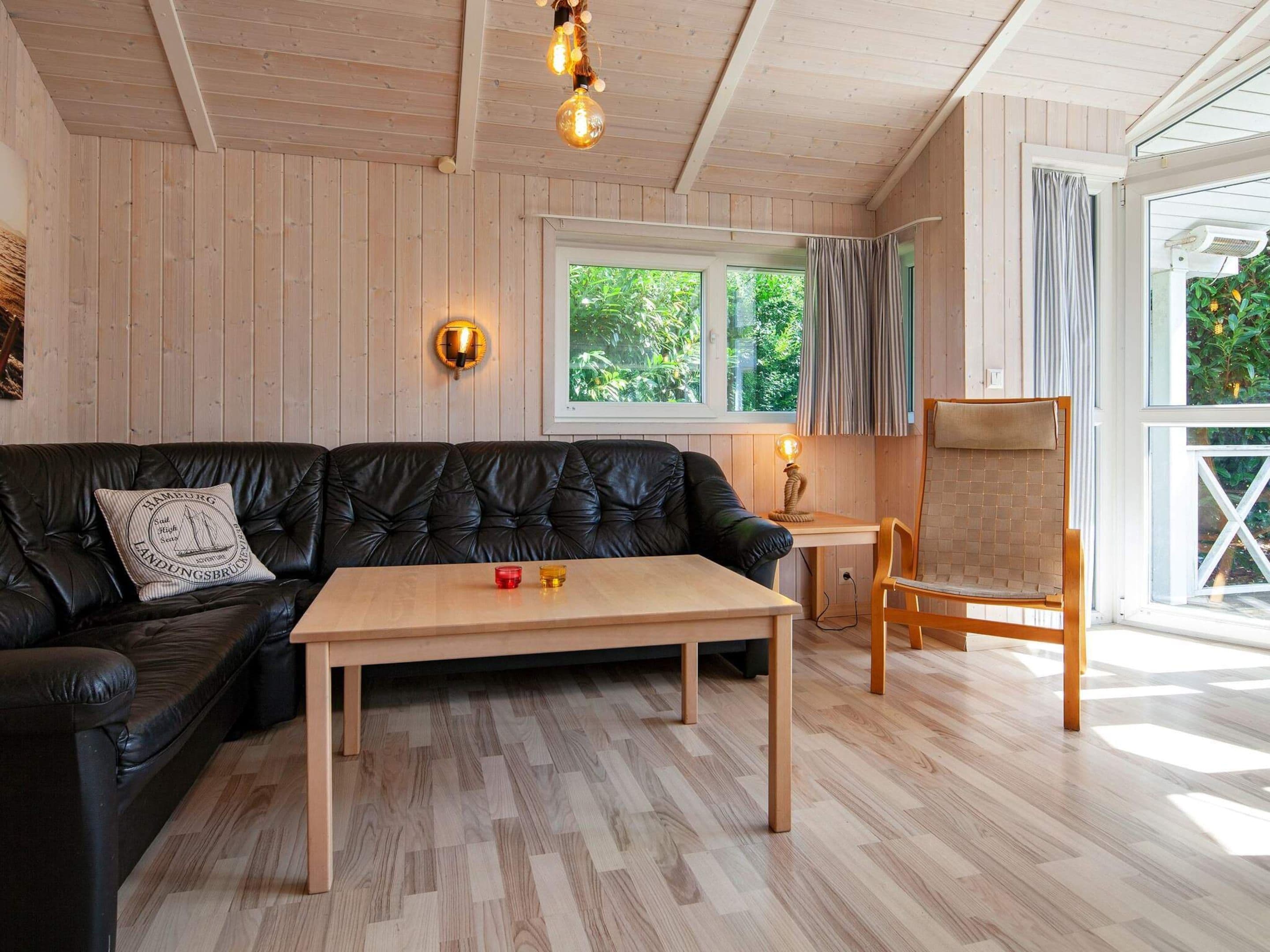 Ein gemütliches Zimmer mit einer schwarzen Ledersofa, einem Holztisch und einem Holzstuhl. Es gibt ein Fenster mit Vorhängen, eine Wandlampe und eine Deckenleuchte.