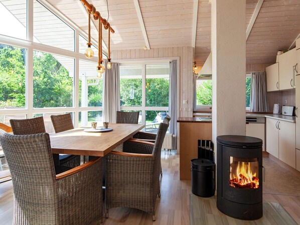 A modern kitchen with a wood-burning stove, large windows, and a dining area with wicker furniture.