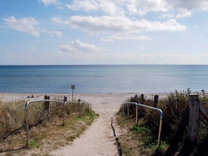 A sandy beach path leading to the sea with a metal railing on the left.