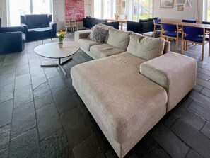 A modern living room with a beige sofa, a round coffee table, and a dining area with blue chairs and a wooden table. - 16 Person Holiday Home in Aabenraa (Aabenraa)