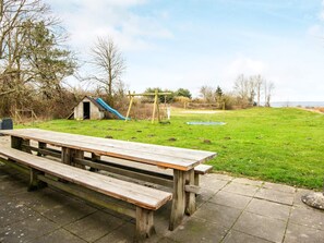 A picnic area with a wooden bench and a small play structure in the background.