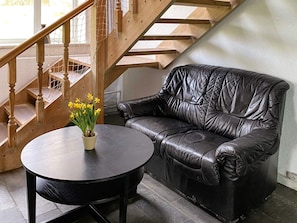 A room with a black leather sofa, a round table with a potted plant, and a wooden staircase. - 16 Person Holiday Home in Aabenraa (Aabenraa)
