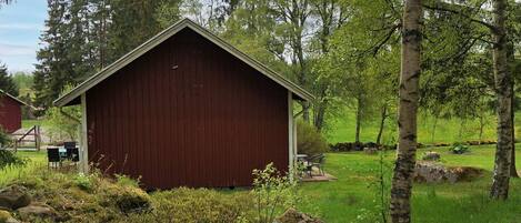 Een rood houten gebouw met een puntige kap, omgeven door een gazon met bomen en rotsen.